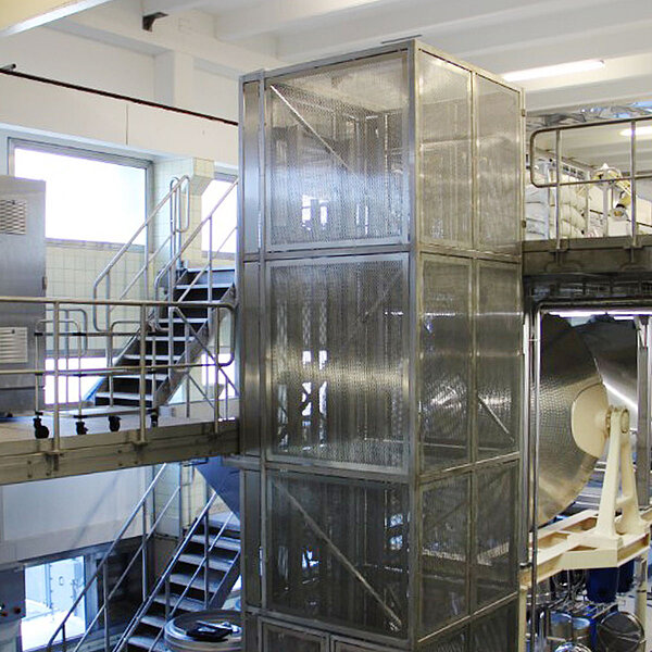 Industrielle Förderanlage mit verglaster Schachtverkleidung, Metalltreppe und Maschinenplattform in einem modernen Produktionsbereich