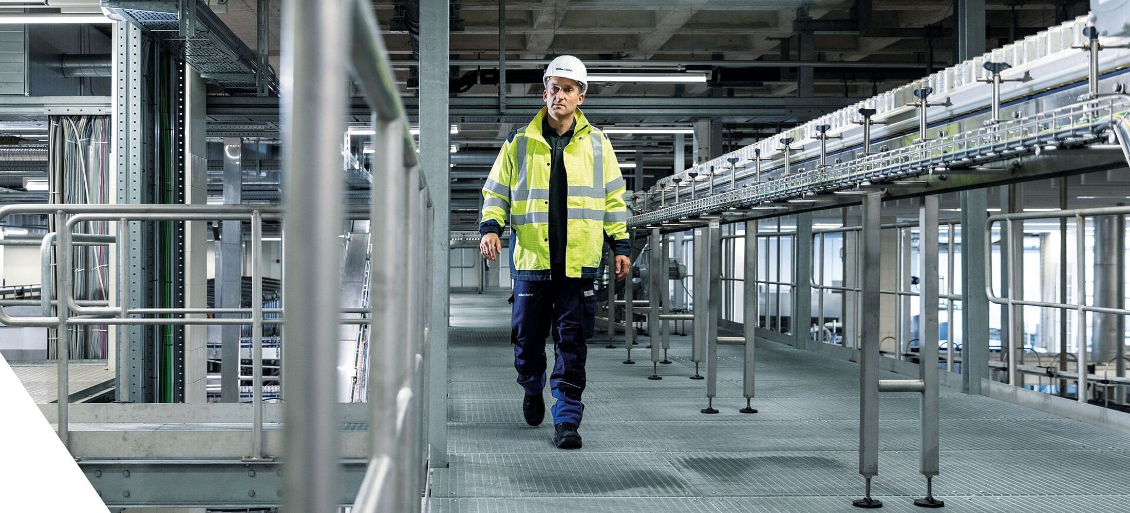 Arbeiter mit Schutzkleidung geht durch eine moderne Industriehalle.