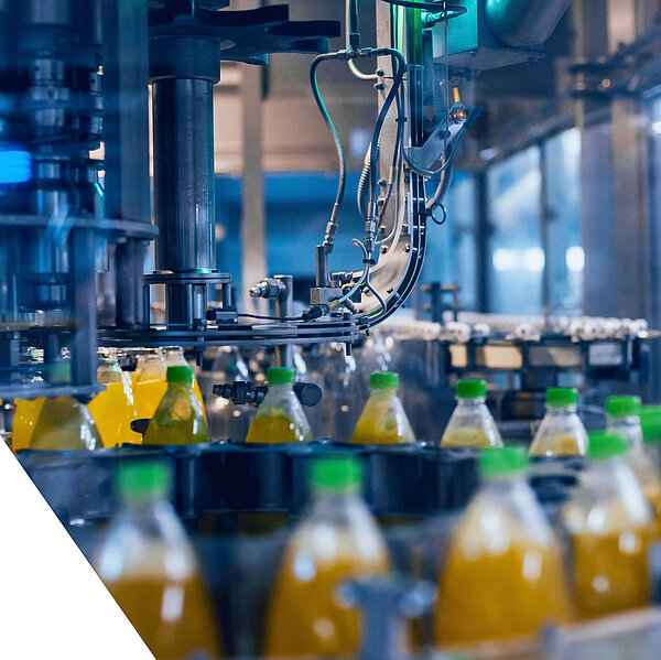 Automatisierte Abfüllanlage in einer Getränkeproduktion, PET-Flaschen mit orangener Flüssigkeit und grünem Deckel auf dem Förderband