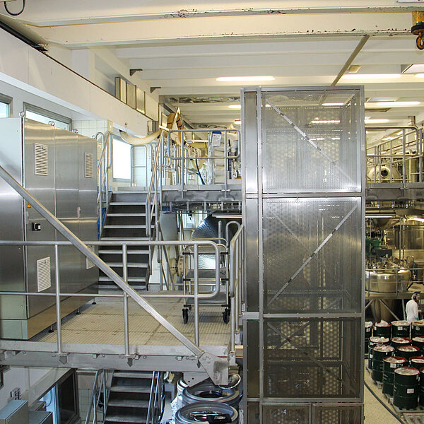 Automatisierte Produktionsanlage mit Fördertechnik und Schutzverkleidung aus Edelstahlgittern in einem Fertigungsraum