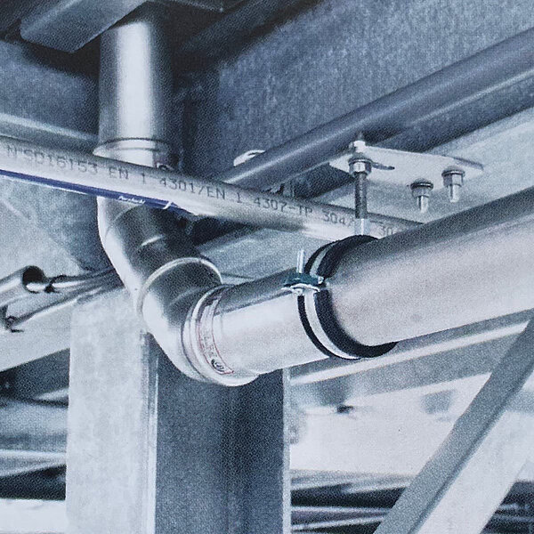 Industrielle Edelstahlrohrleitung unter einer Metallkonstruktion mit Flanschverbindung und Halterungen
