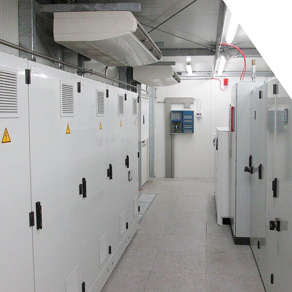 Technikraum mit weißen Schaltschrankanlagen und Lüftungssystem an der Decke.