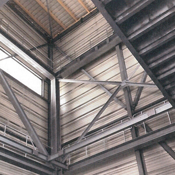 Blick nach oben auf die Stahltragkonstruktion und Dachstruktur einer Industriehalle mit diagonalen Verstrebungen und Gitterträgern