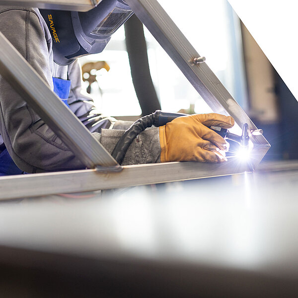 Schweißer mit Schutzkleidung und Handschuhen bei der Arbeit an einer Metallkonstruktion mit Lichtbogen.