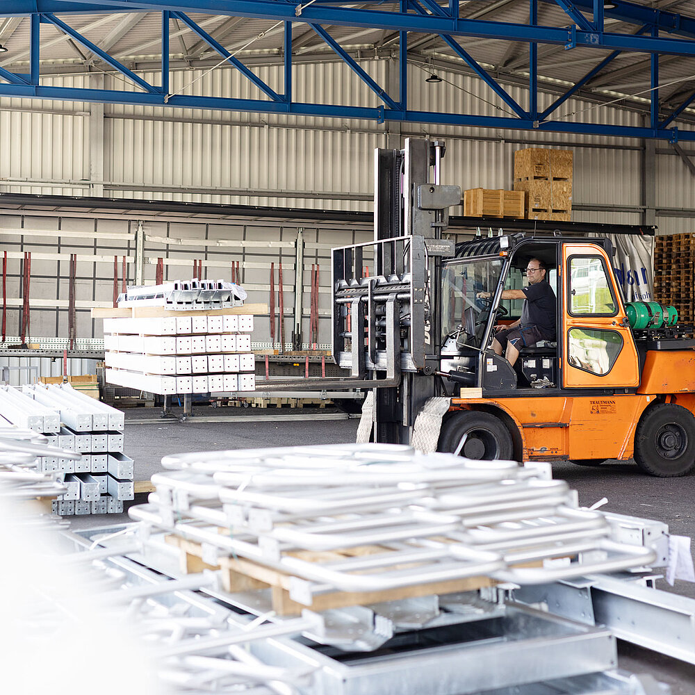 Staplerfahrer transportiert Metallplatten in einer Industriehalle mit Hochregalen und Stahlkonstruktion