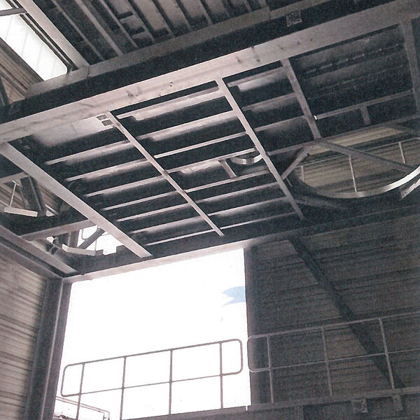 Blick von unten auf eine industrielle Stahlbaukonstruktion mit Deckenrahmen und Geländer in einer Produktionshalle